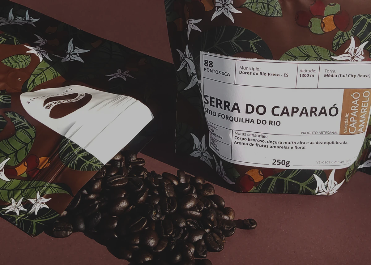 Detalhe de embalagem Grão Café.com com rótulo Serra do Caparaó junto aos grãos de café